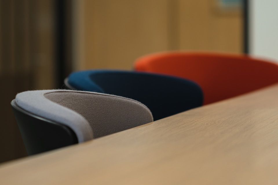 Three colorful chairs lined up at a light-colored table: gray, blue, and orange.