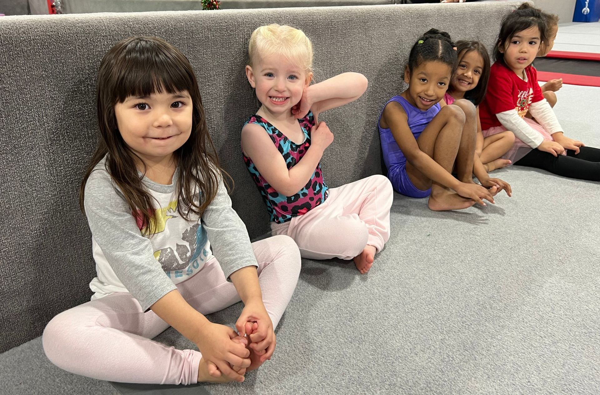 A group of young girls are sitting on the floor in front of a mirror.