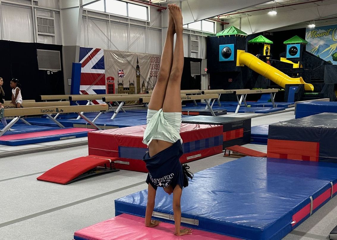 A female gymnast is standing on a balance beam.