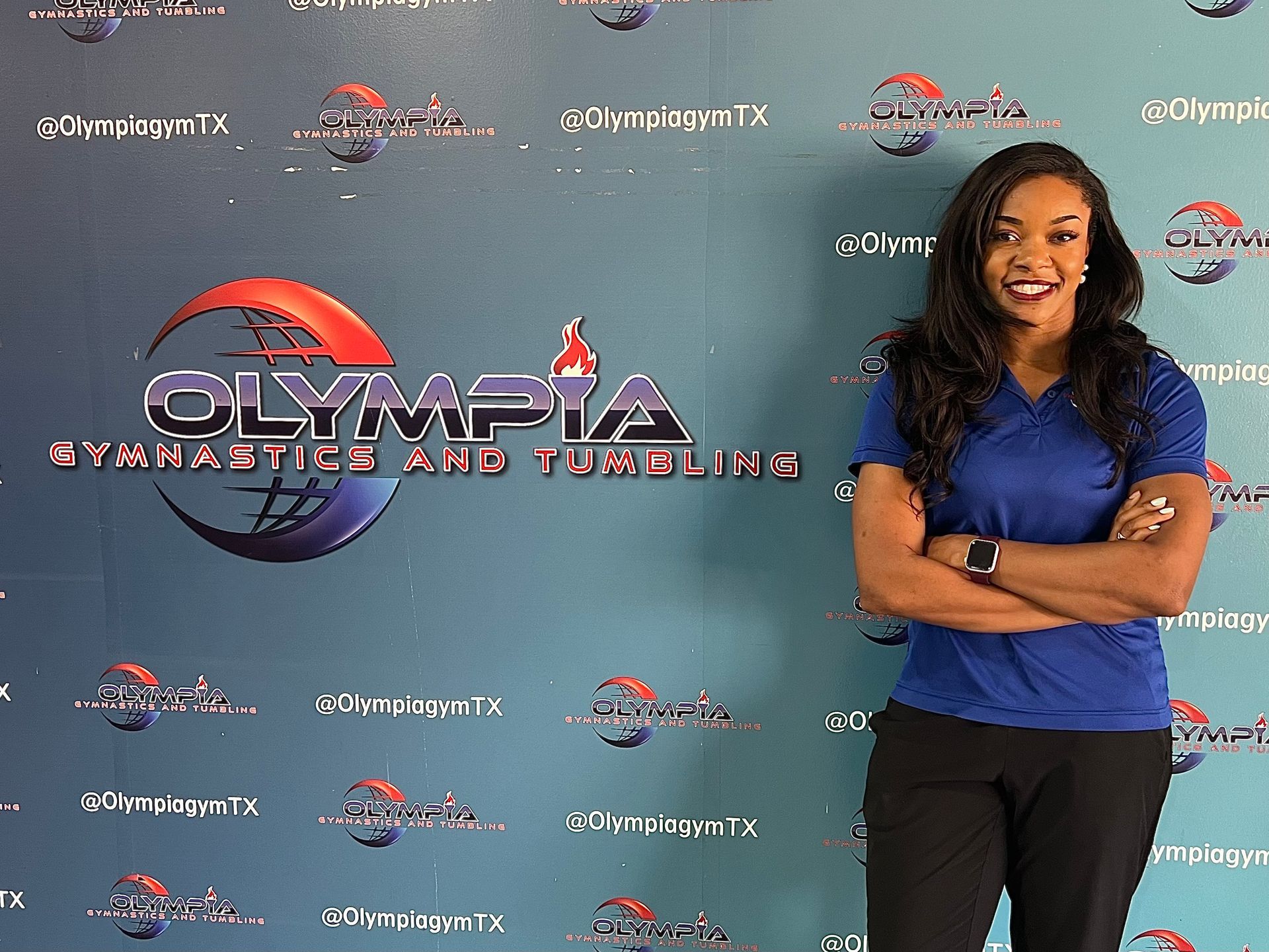 A woman is standing in front of a wall that says olympia gymnastics and tumbling
