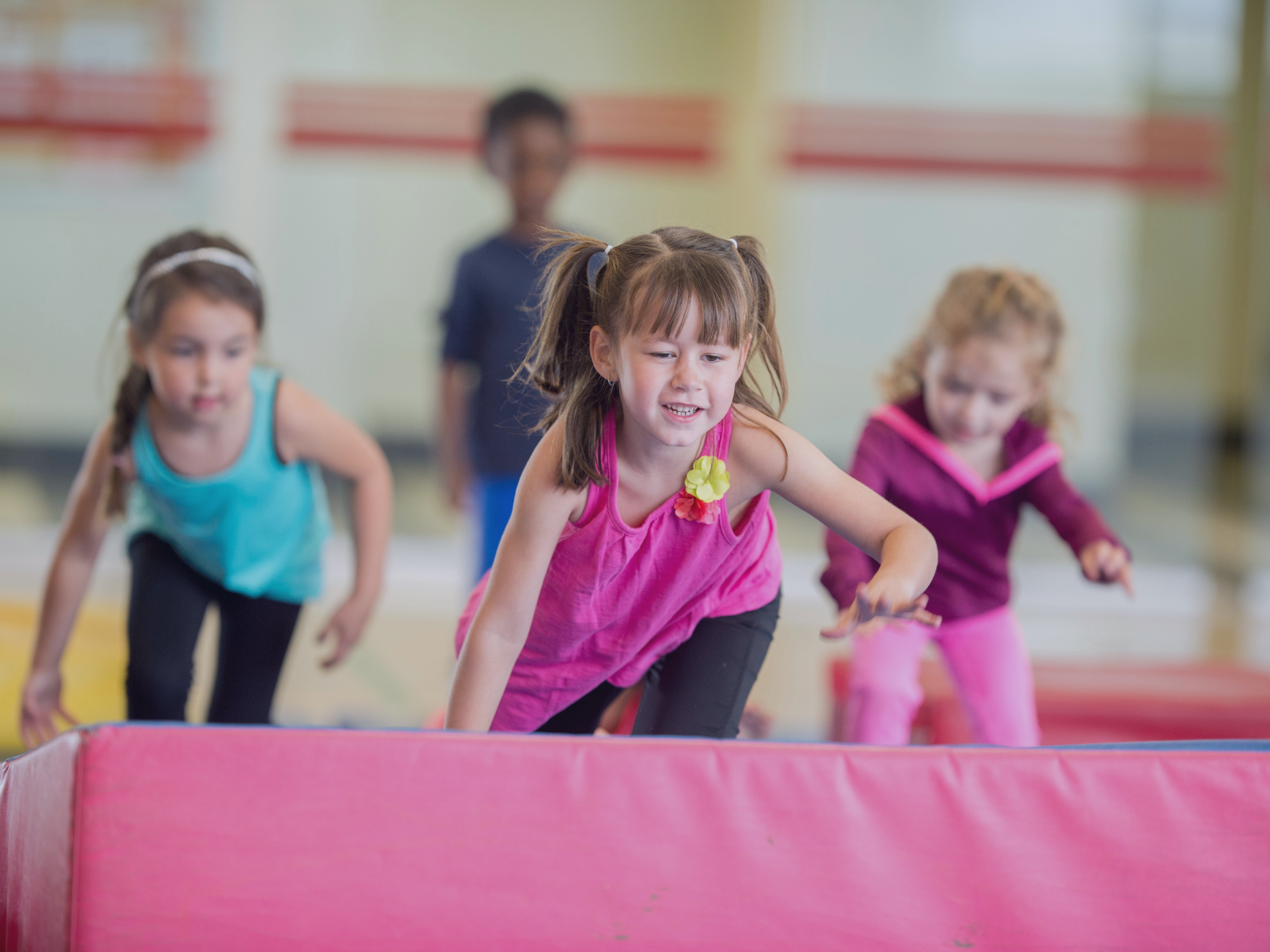 Young children participating in a preschool gymnastics class, climbing over padded equipment inside 