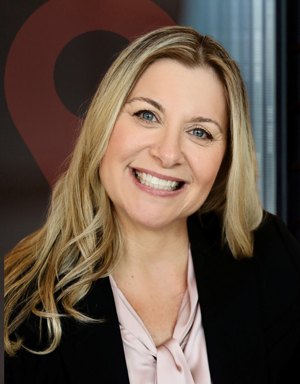A woman wearing a black jacket and a pink shirt is smiling for the camera.