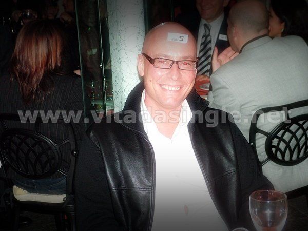 Un uomo con gli occhiali e una targhetta con il nome sorride alla telecamera