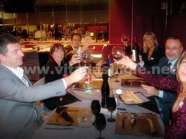 Un gruppo di persone è seduto ad un tavolo e brinda con calici di vino