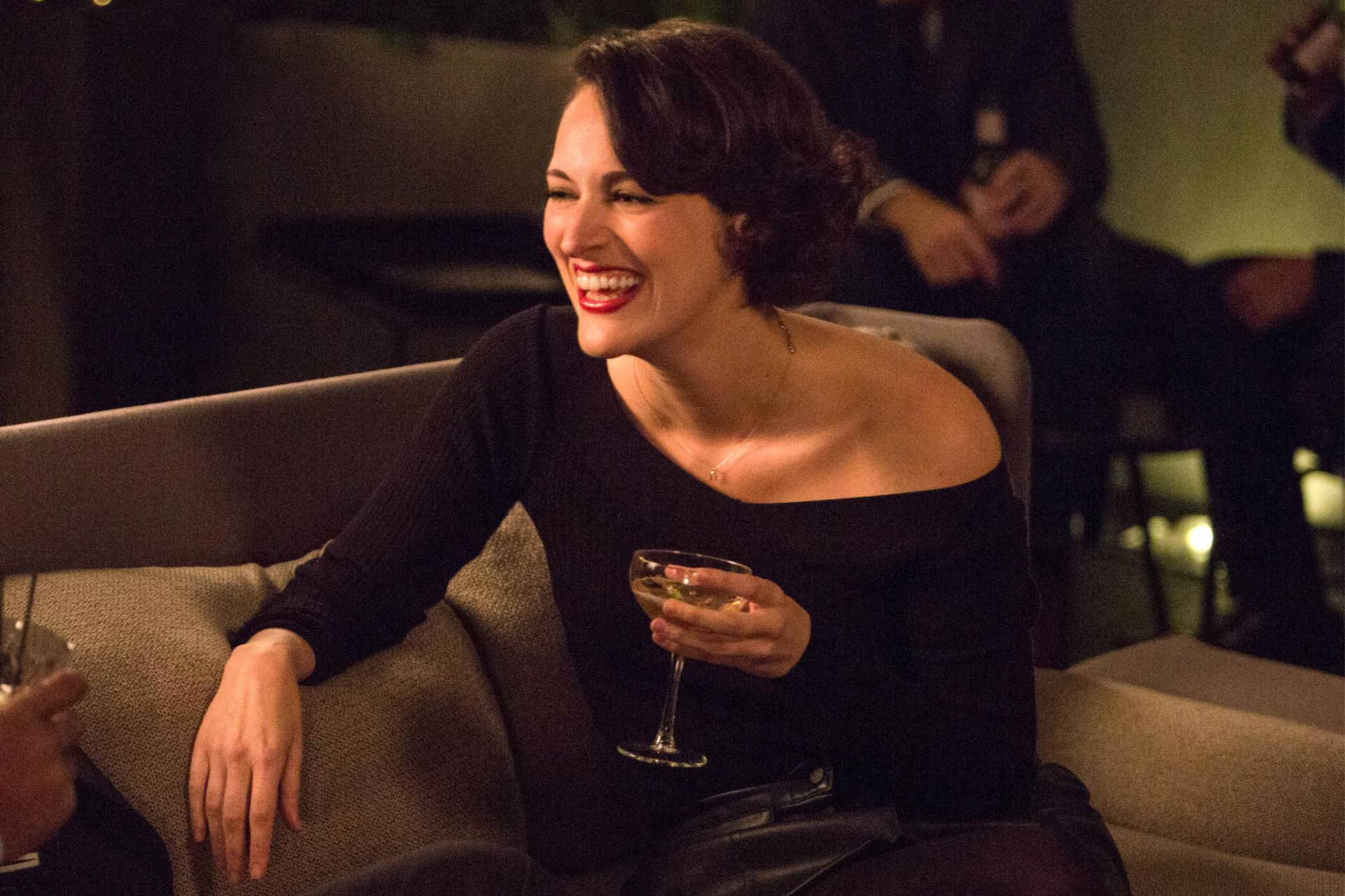 una donna è seduta su un divano con in mano un bicchiere di champagne e ride .
