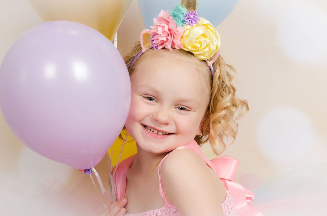 A little girl is holding a purple balloon and smiling.