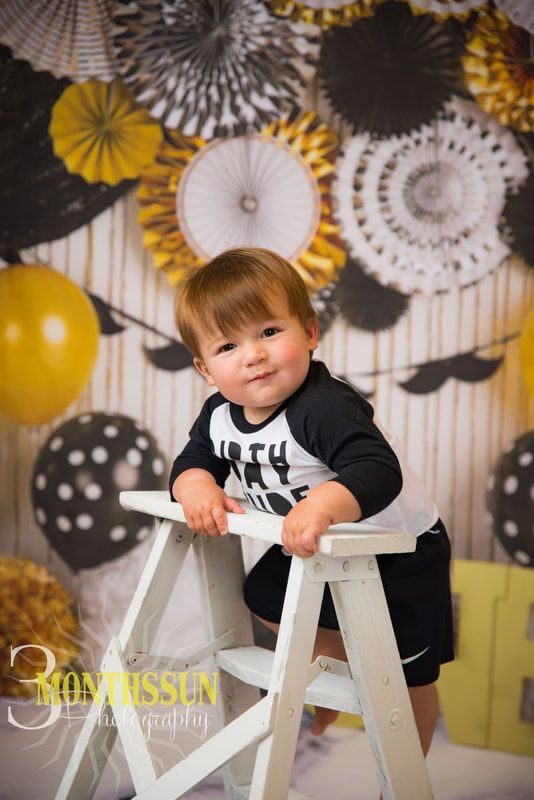 A baby boy is sitting on a white ladder in front of a wooden wall.