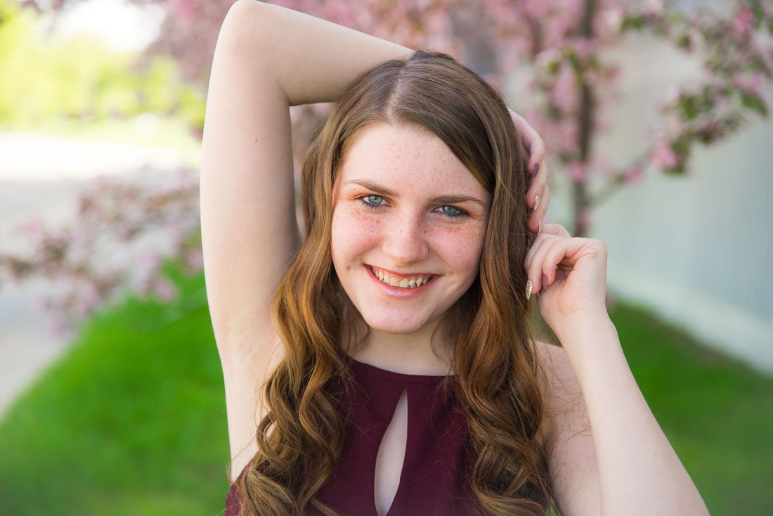 A young woman is smiling with her hand in her hair in front of a cherry blossom tree.