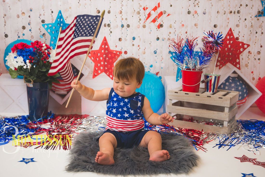 A baby is sitting on the floor holding an american flag.