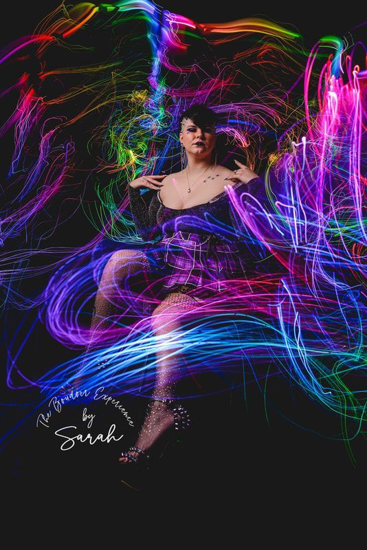 A woman is sitting in front of a colorful light painting.