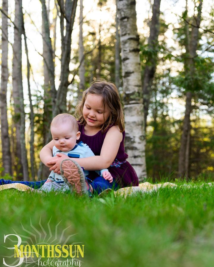 A little girl is holding a baby in her arms while sitting in the grass.