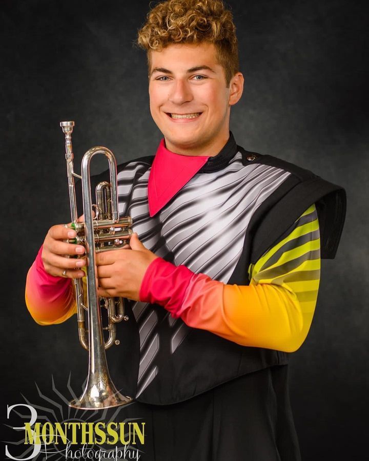 A young man in a marching band uniform is holding a trumpet