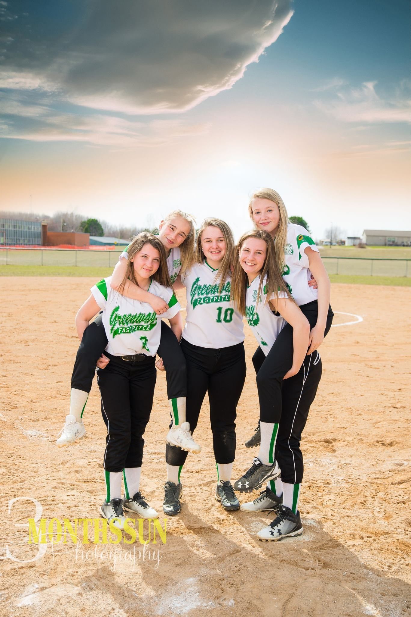 A group of girls are posing for a picture on a softball field.