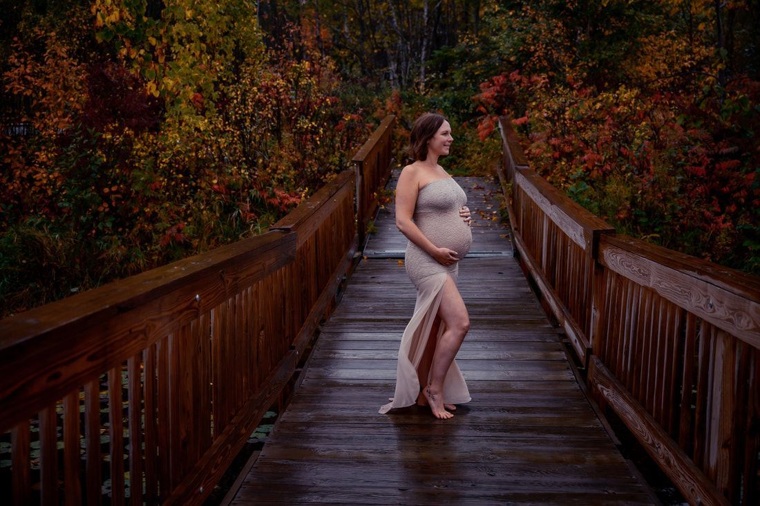A pregnant woman is standing on a wooden bridge in the rain.