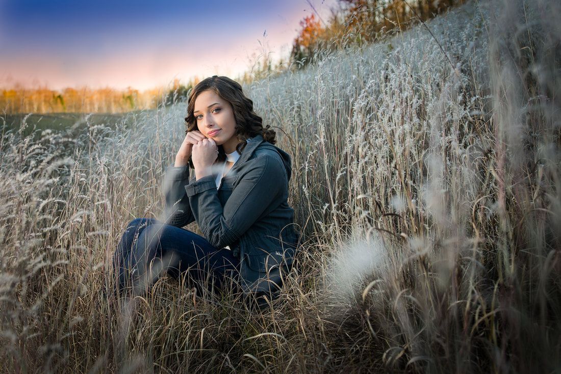 A woman is sitting in a field of tall grass.