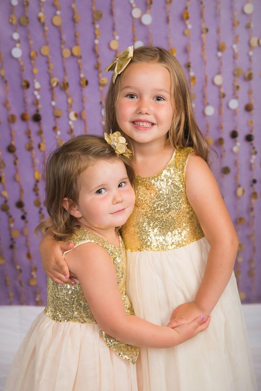 Two little girls are hugging each other in front of a purple background.