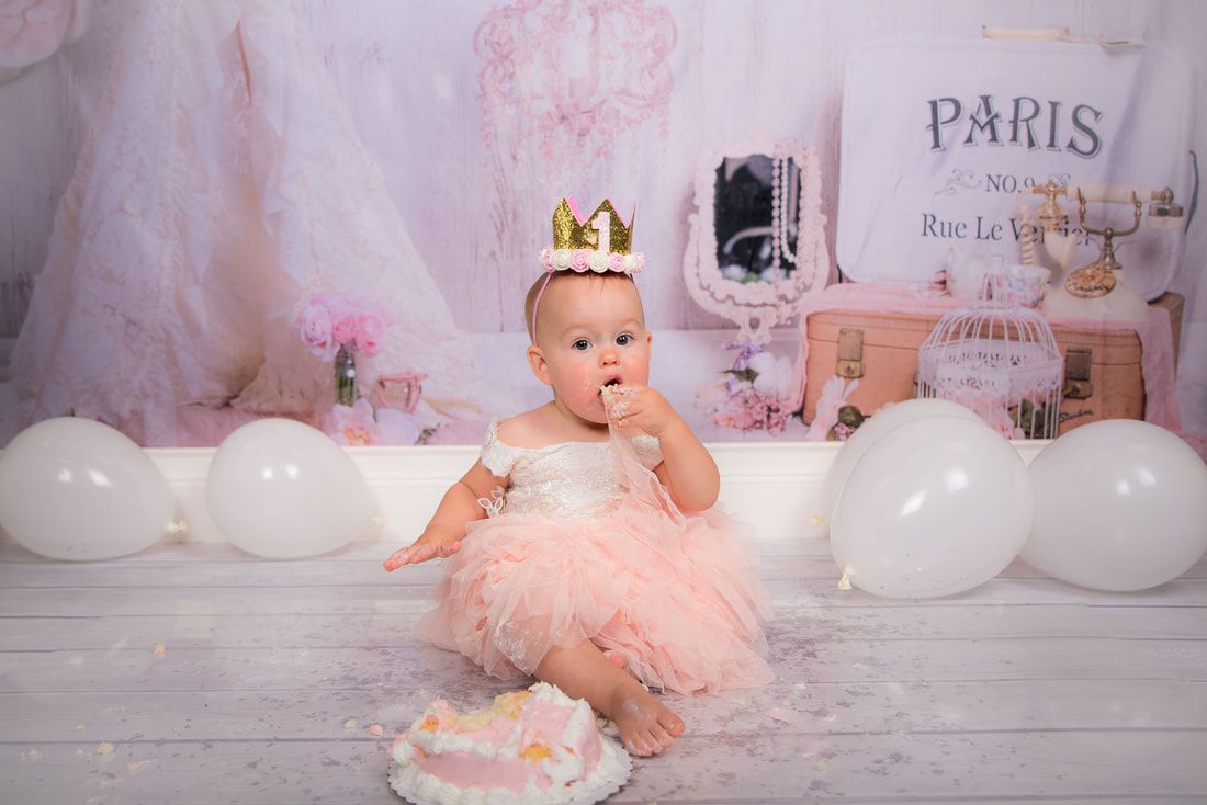 A baby girl is sitting on the floor eating a cake.