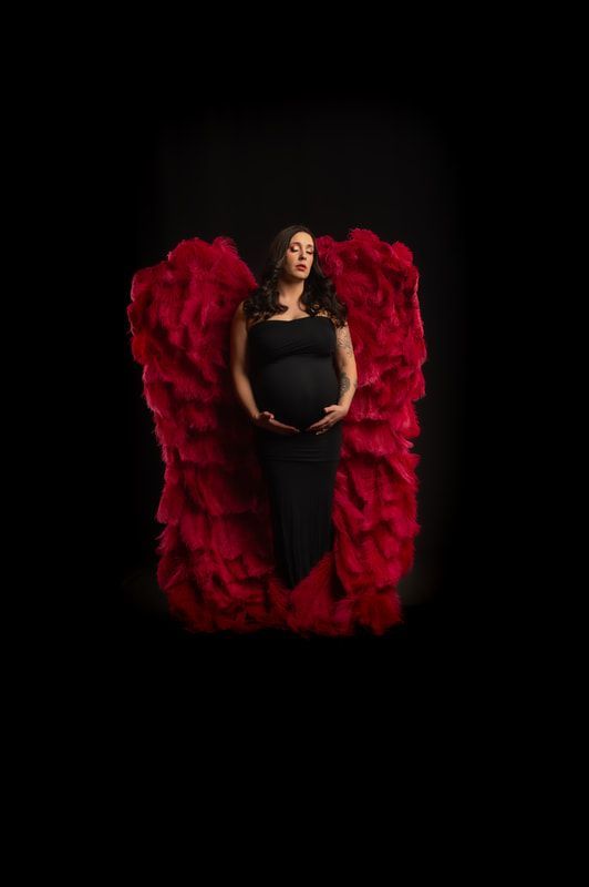 A pregnant woman in a black dress is surrounded by red feathers.