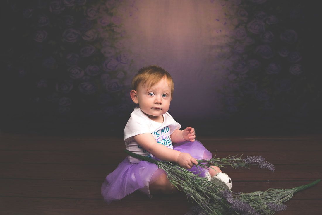 A baby girl is sitting on the floor holding a bouquet of lavender flowers.
