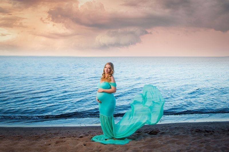 A pregnant woman in a blue dress is standing on the beach.