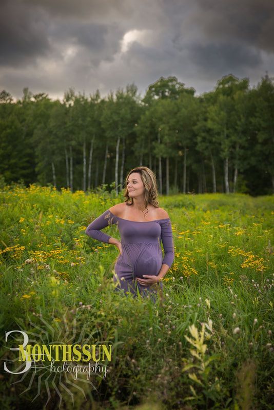 A pregnant woman in a purple dress is standing in a field of flowers.
