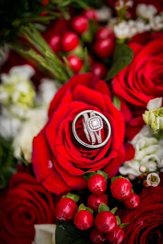 A wedding ring is sitting on top of a red rose.