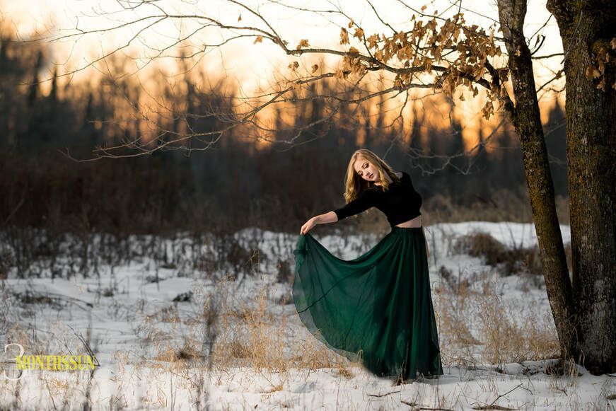 A woman in a long green skirt is dancing in a snowy field.