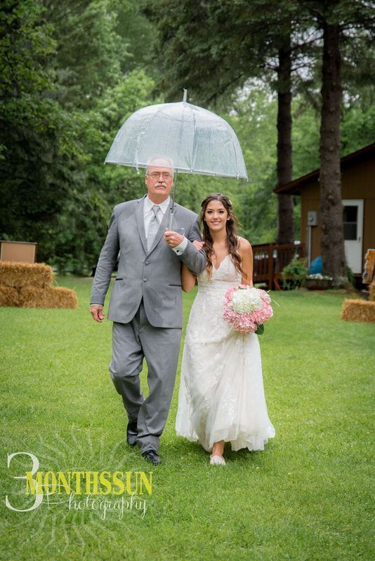 A bride and her father are walking down the aisle under an umbrella.