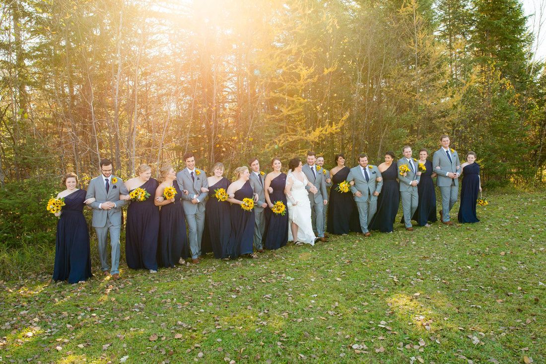 A bride and groom are posing for a picture with their wedding party in a field.