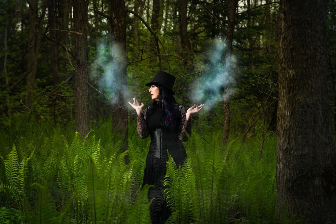 A woman in a witch costume is standing in the woods with smoke coming out of her hands.