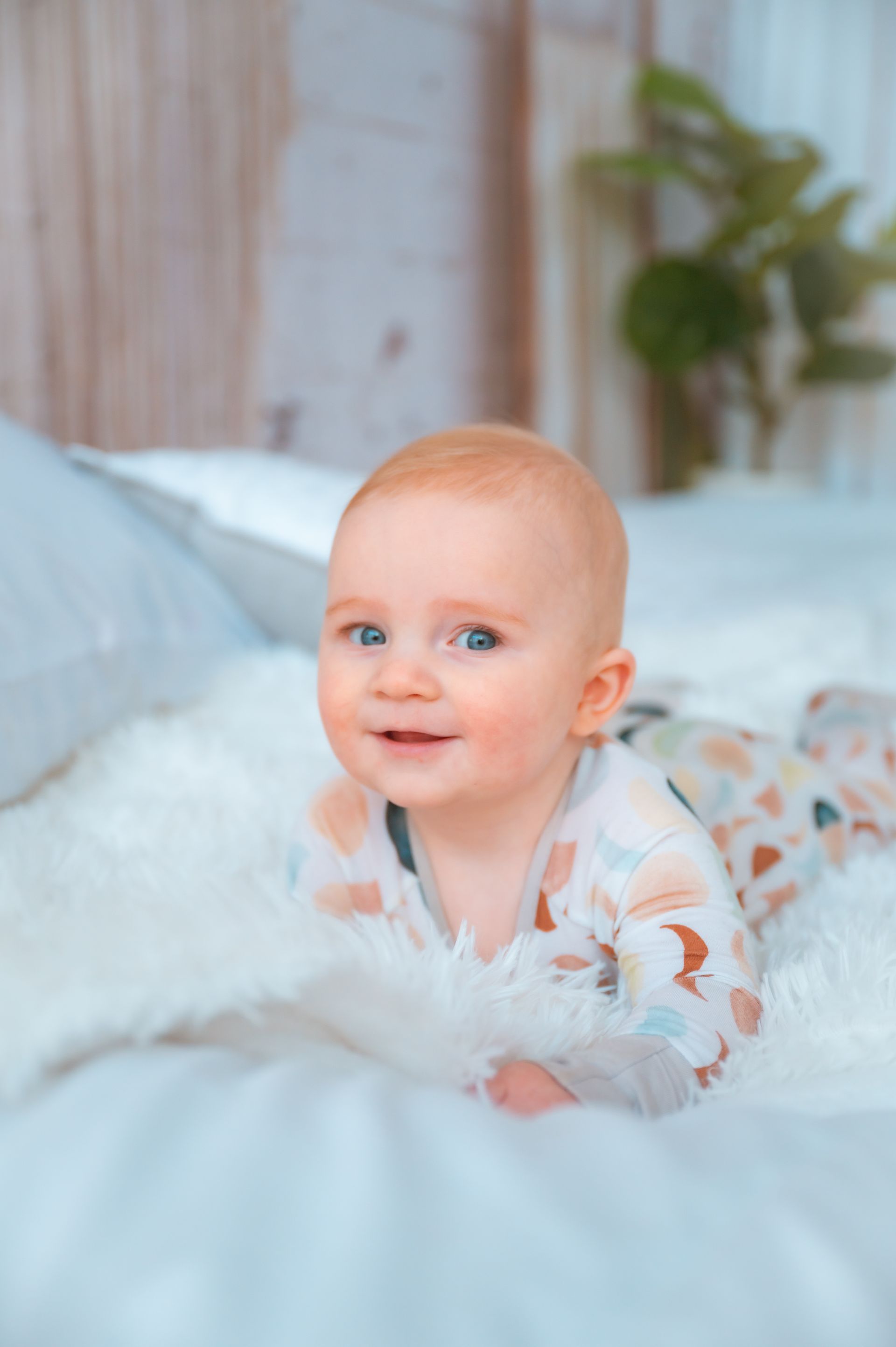 A baby is laying on his stomach on a bed and smiling.