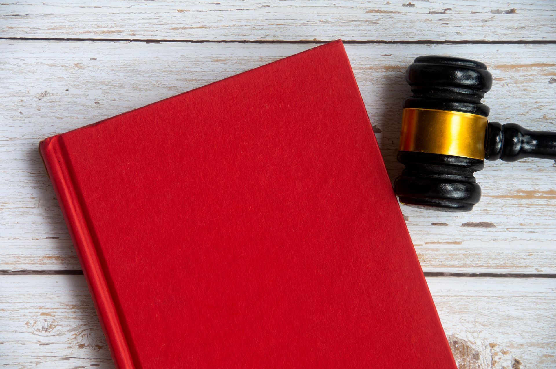 A red book and a judge 's gavel on a wooden table.