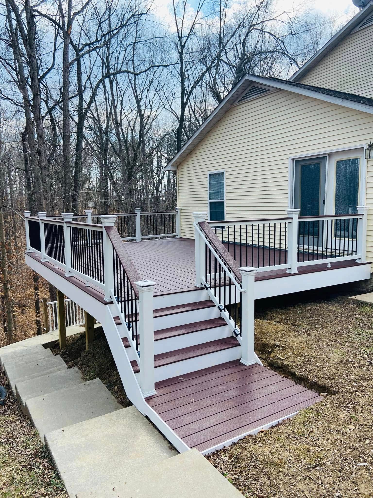 A composite deck with stairs and railings attached to a two-story home on a hillside.