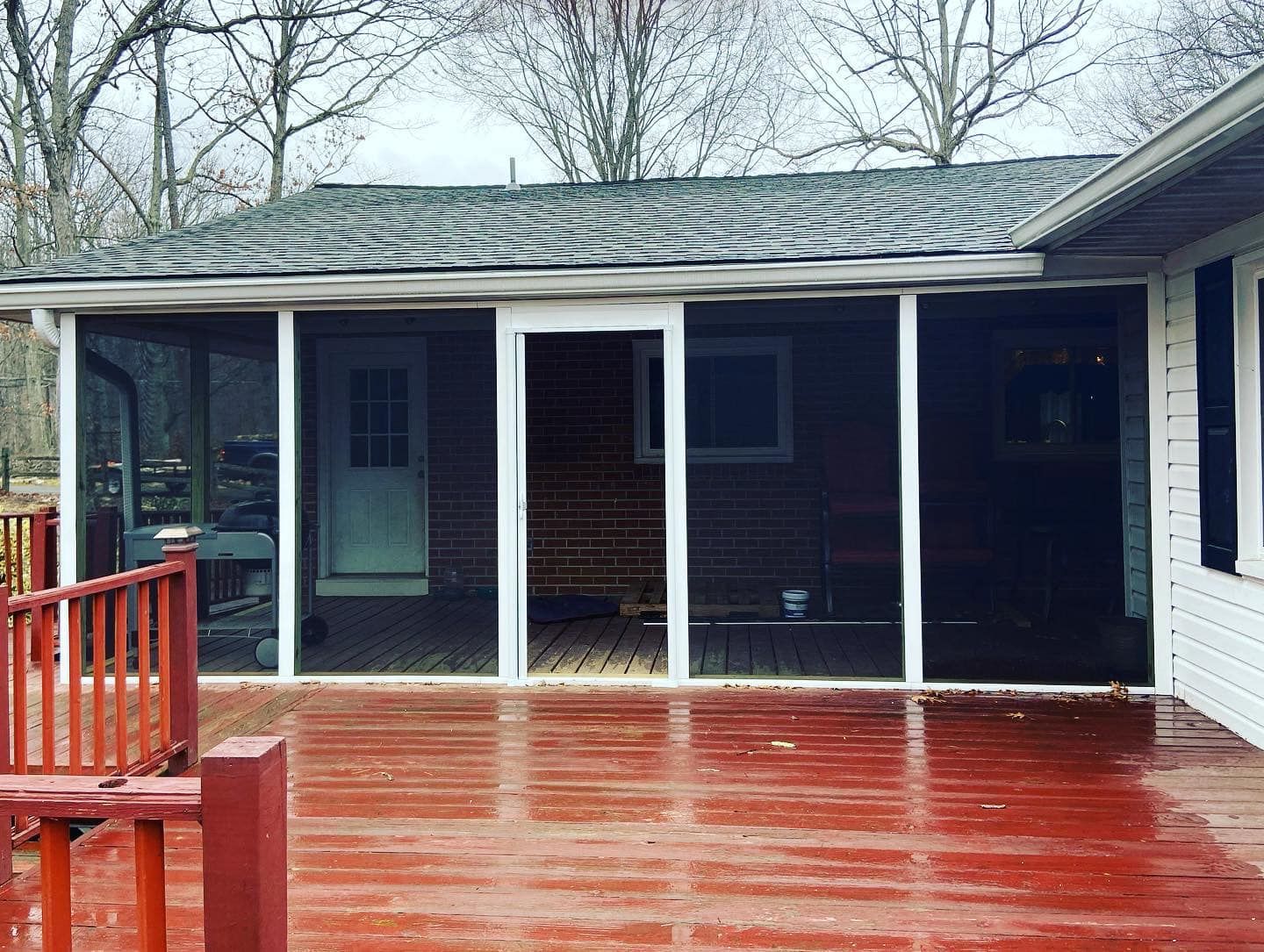 A screened in porch with a red deck next to a house.