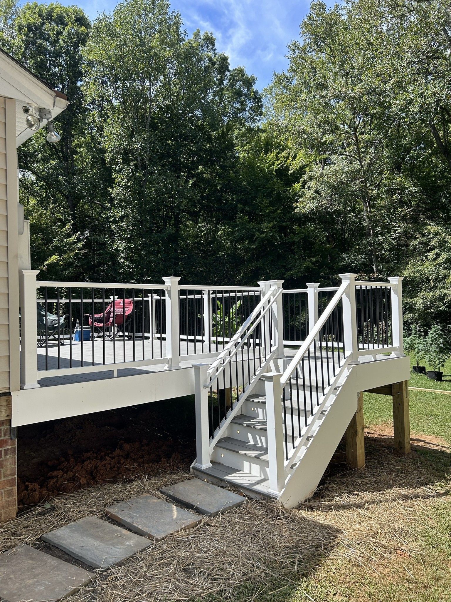 A white deck with stairs leading up to it is in the backyard of a house.