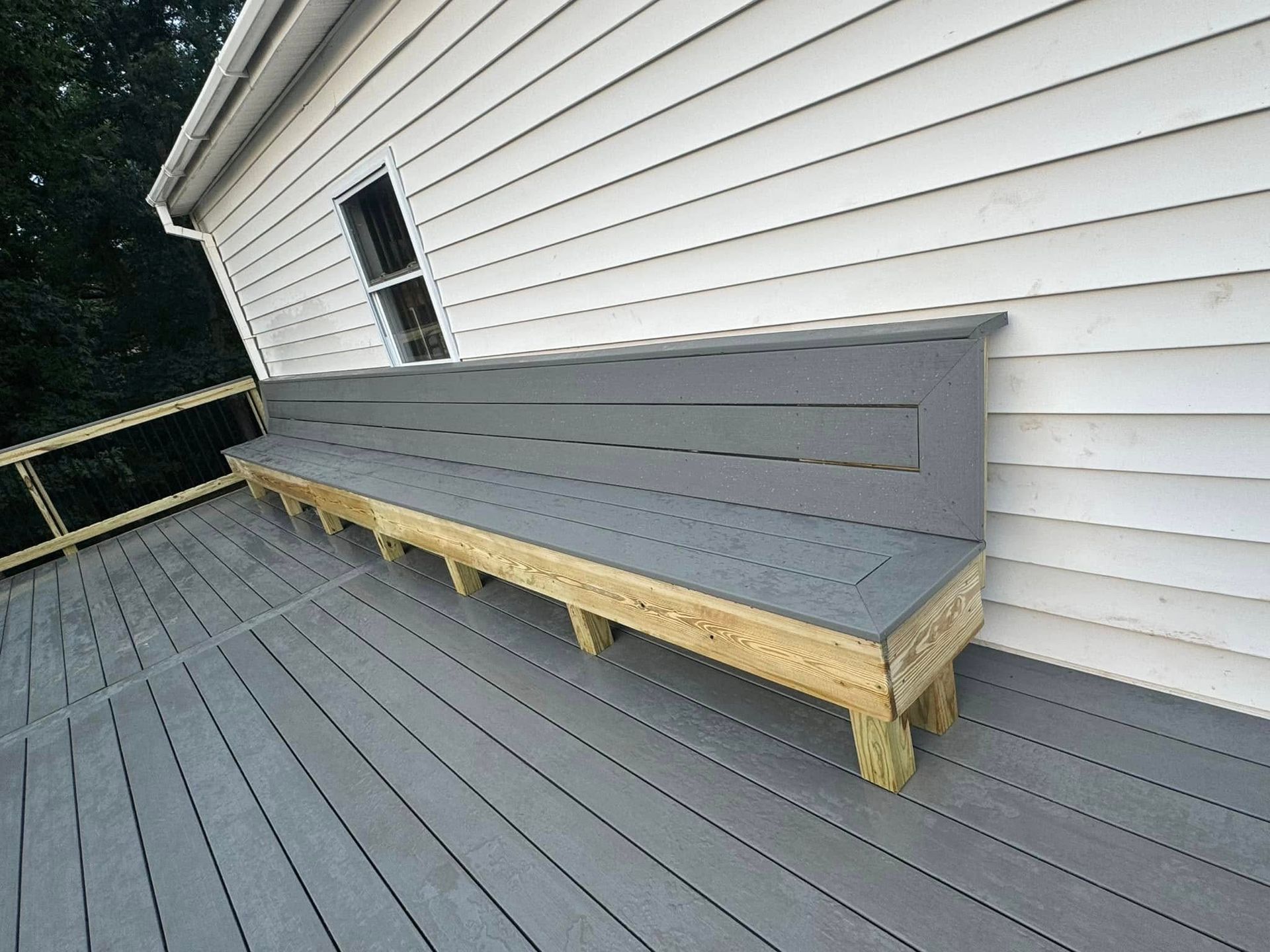 A wooden bench on a deck next to a white house