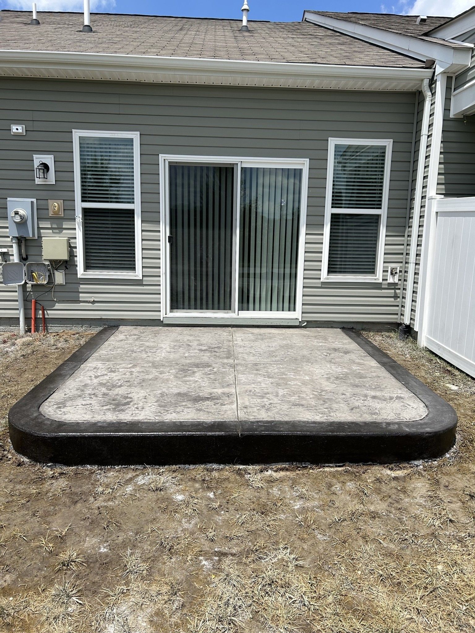 A concrete patio in front of a house with a sliding glass door.