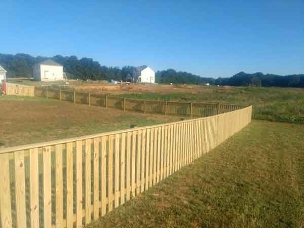 A wooden fence surrounds a grassy field with houses in the background.
