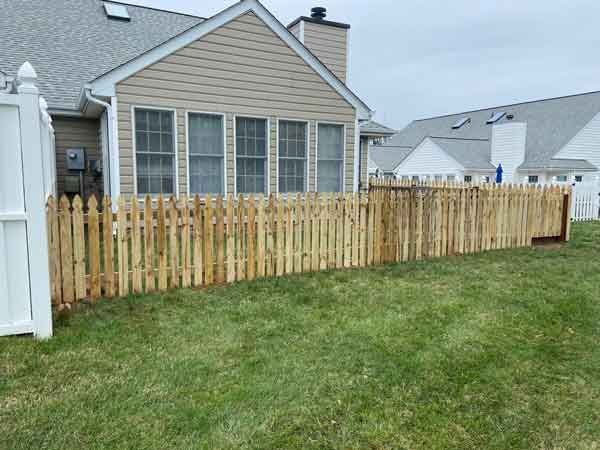 A wooden picket fence is in the backyard of a house.