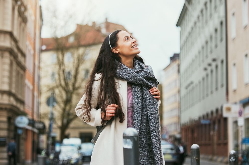 A woman in a white coat and scarf is walking down a city street.