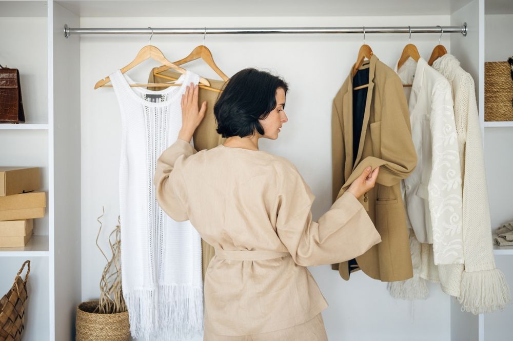 A woman is standing in a closet looking at clothes.