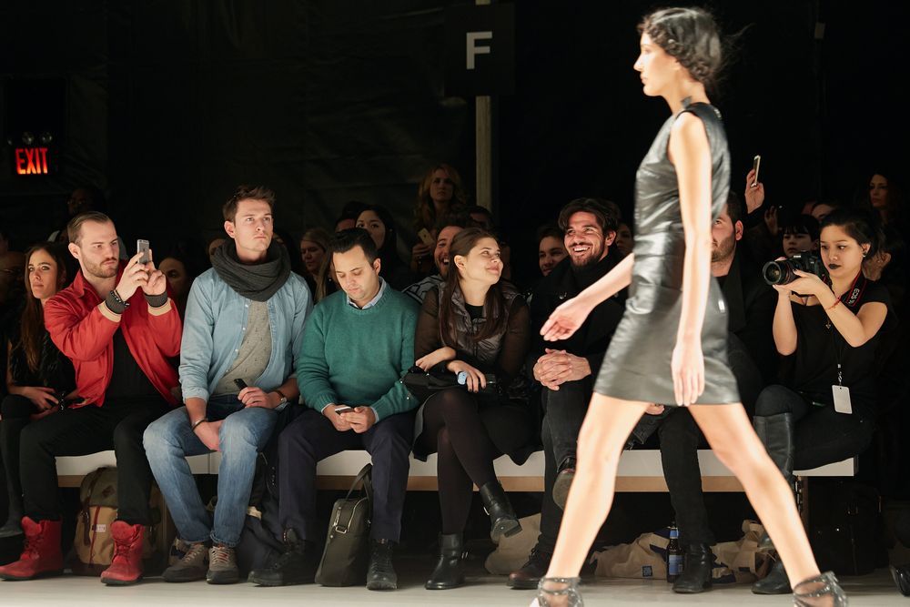 A group of people are watching a model walk down the runway at a fashion show.