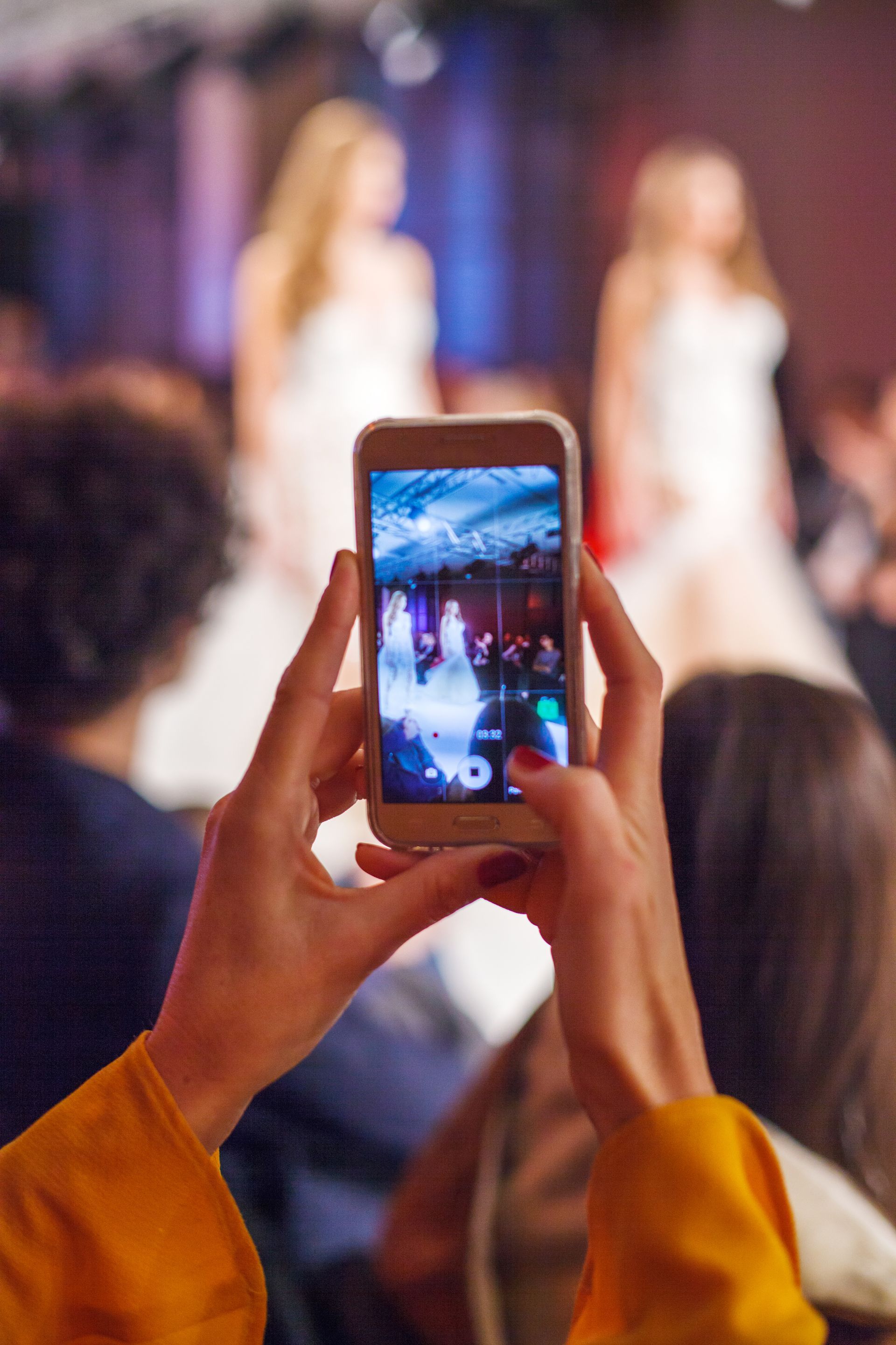 a person is taking a picture of a fashion show with a cell phone demonstrating the power of building a brand through runway shows