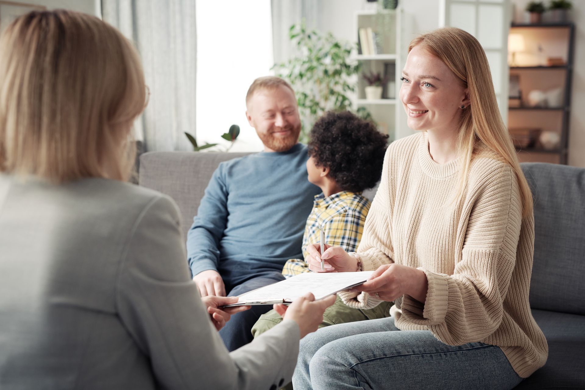 Three people talking in a bright living room, holding a document and smiling.