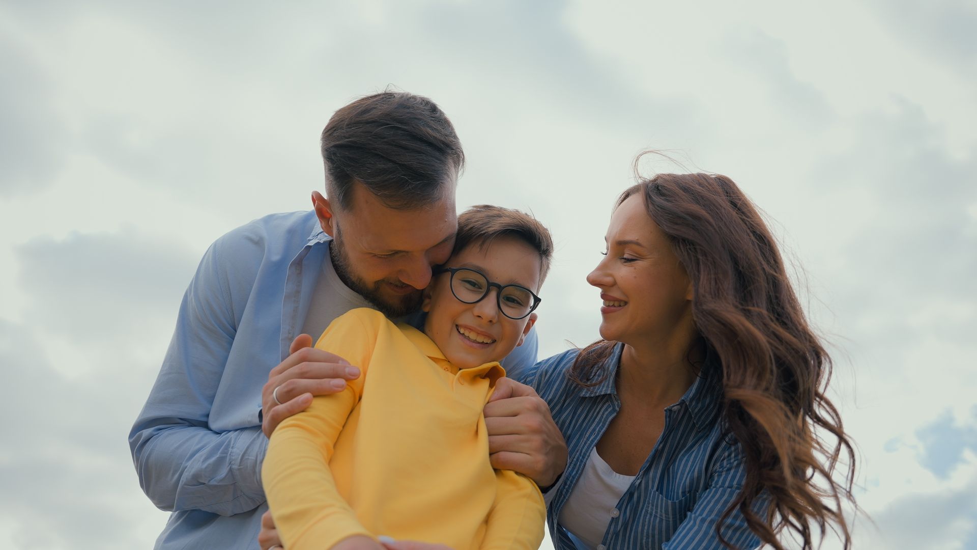 Three people smiling outdoors, with two leaning in to hug the person in the center.
