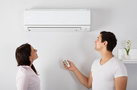 A Couple Looks Up at a Wall-mounted Air Conditioner as the Man Holds a Remote — Carl Voss-Electrician In Urangan, QLD