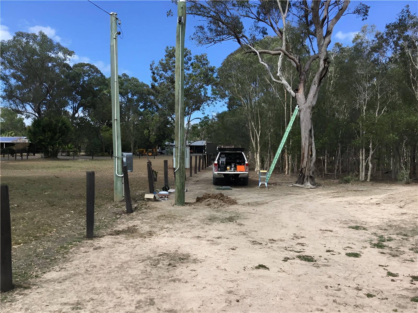 A Utility Truck Parked on a Dirt Road Near Power Poles and Trees — Carl Voss-Electrician In Urangan, QLD