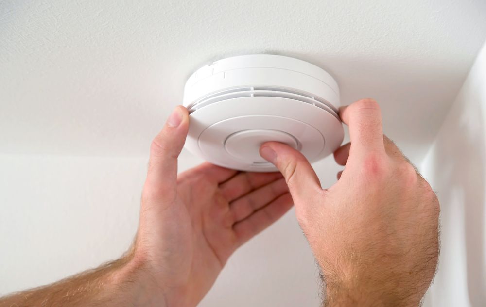 Hands Installing a White Smoke Detector on a White Ceiling — Carl Voss-Electrician In Urangan, QLD