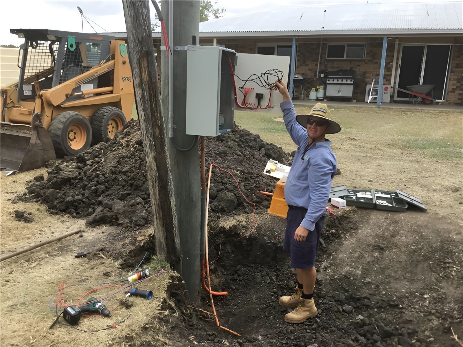 Man in Shorts by Utility Pole, Pointing at a Box — Carl Voss-Electrician In Urangan, QLD