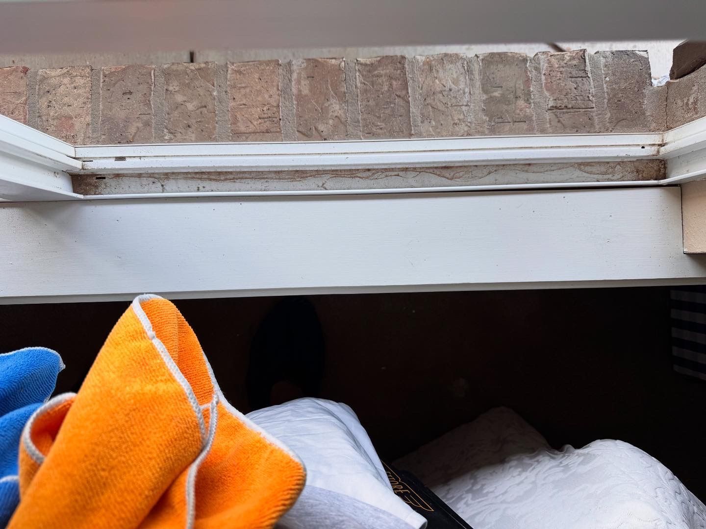 White window frame against brick, with colorful cloths in foreground.